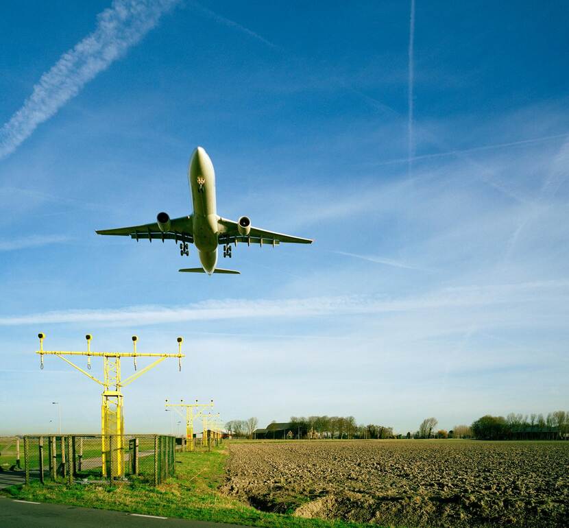 Afbeelding met opstijgend vliegtuig met blauwe lucht en landbouwgrond als achtergrond